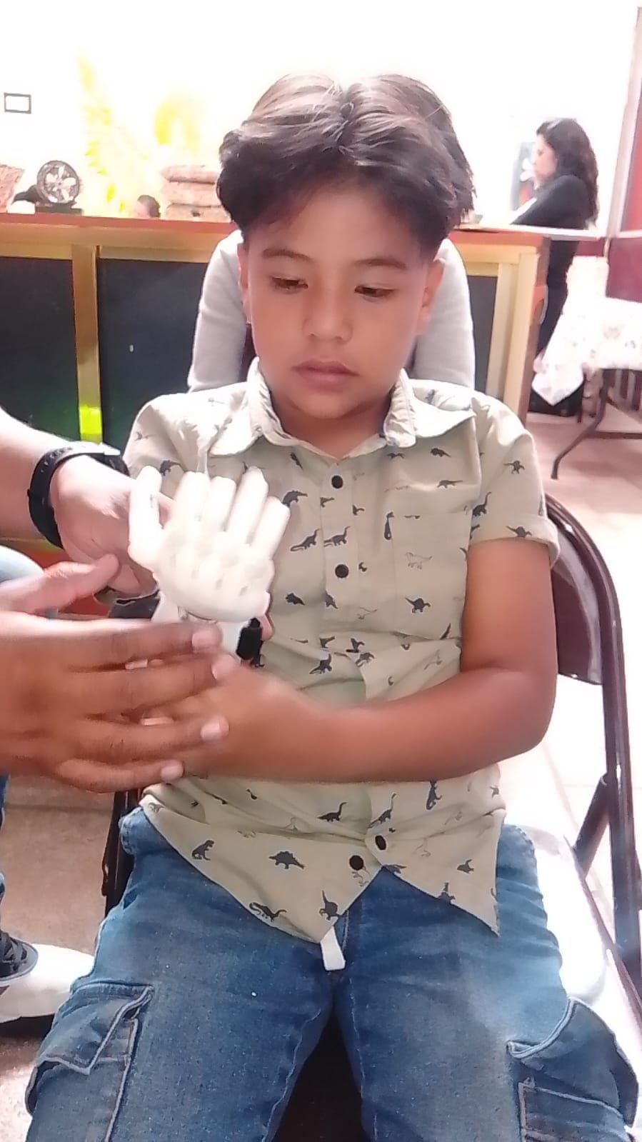 A boy tries on his new 3D-printed hand while a volunteer fits it to his arm.